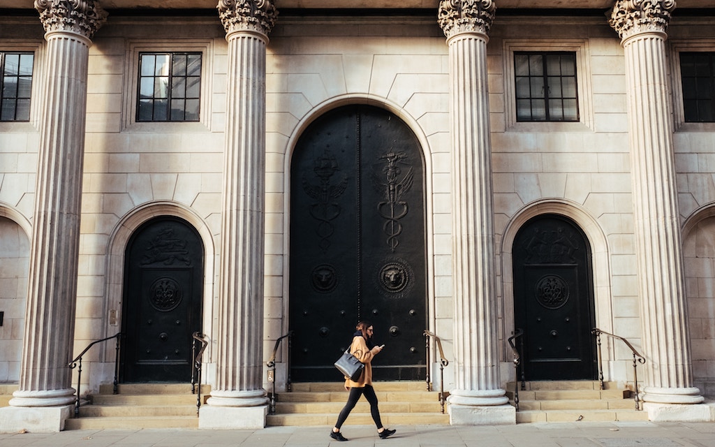 Woman walking in front of the Bank of England, looking at her phone